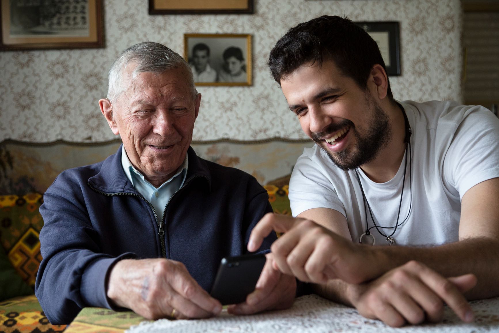 Adult Grandson Showing To His Granddad How To Use The Phone With Touchscreen